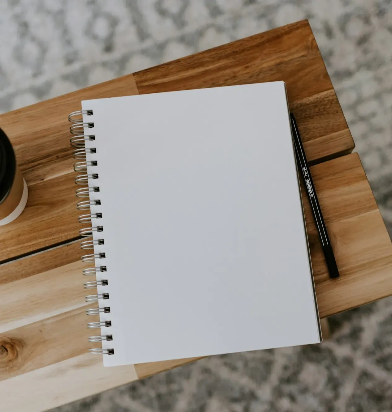Open spiral notebook and coffee cup on a wooden board