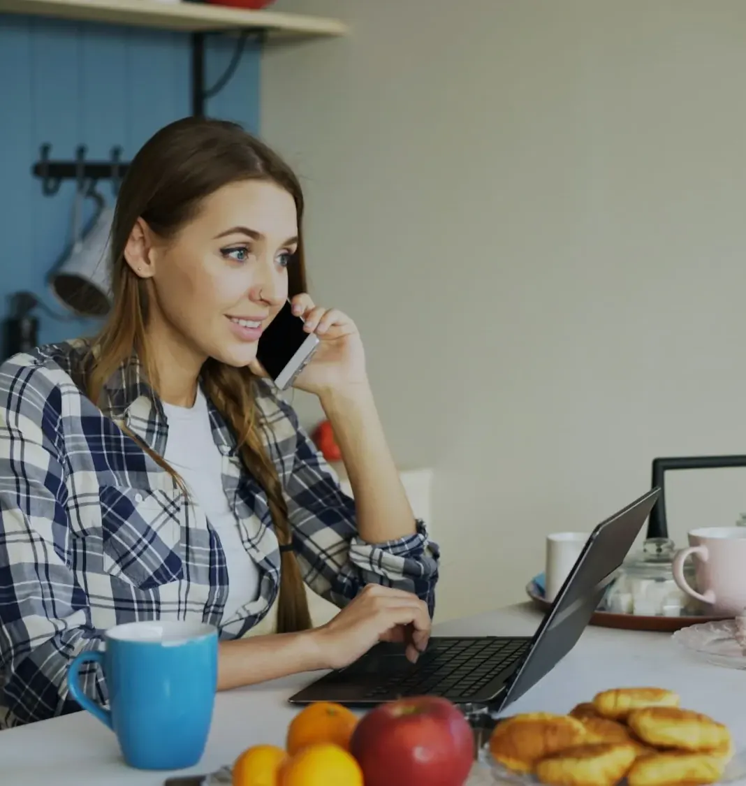 Woman on a phone call at a kitchen table with a laptop