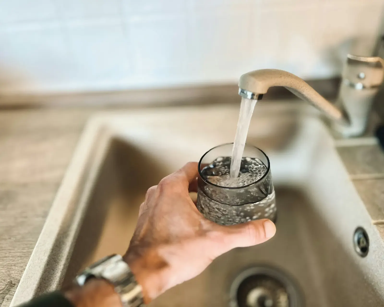 Hand filling a glass of water at a stainless steel sink
