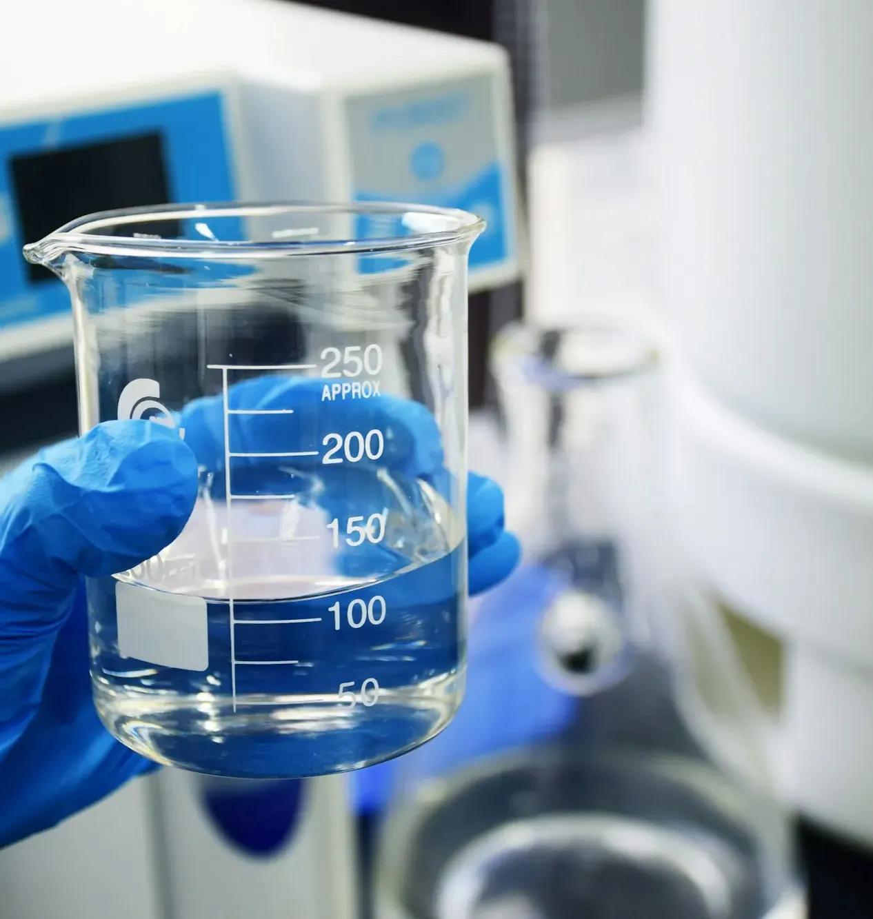 Gloved hand holding a beaker beside laboratory equipment